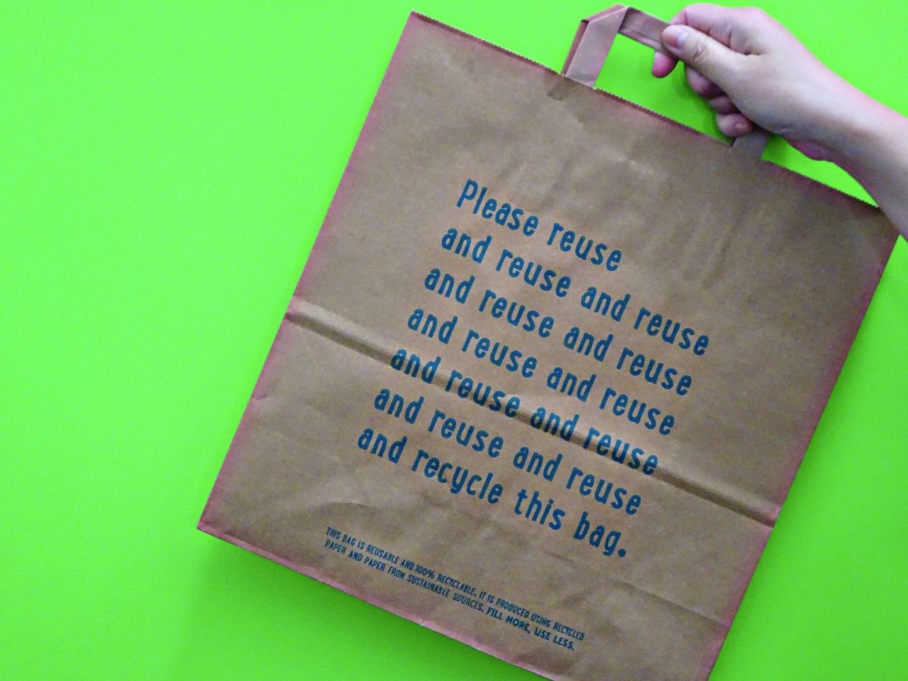 A flat handle brown kraft paper bag with green background with the words reuse written on it